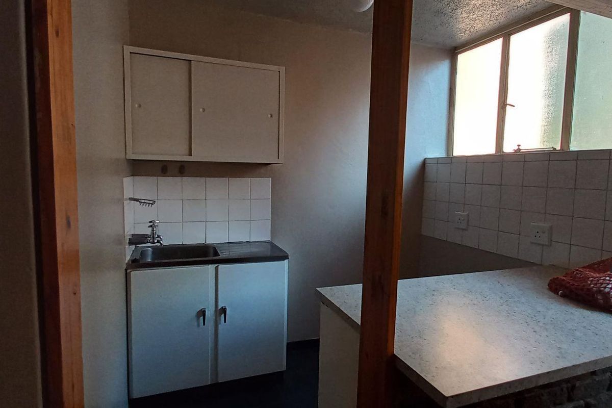 A compact, dated kitchen area featuring built-in cabinetry, a sink with tiled splashback, and a functional countertop space.