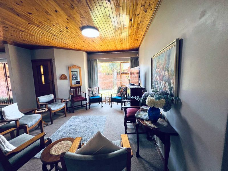 A living room featuring a knotty pine tongue and groove ceiling, carpeted flooring, and large windows providing natural light.