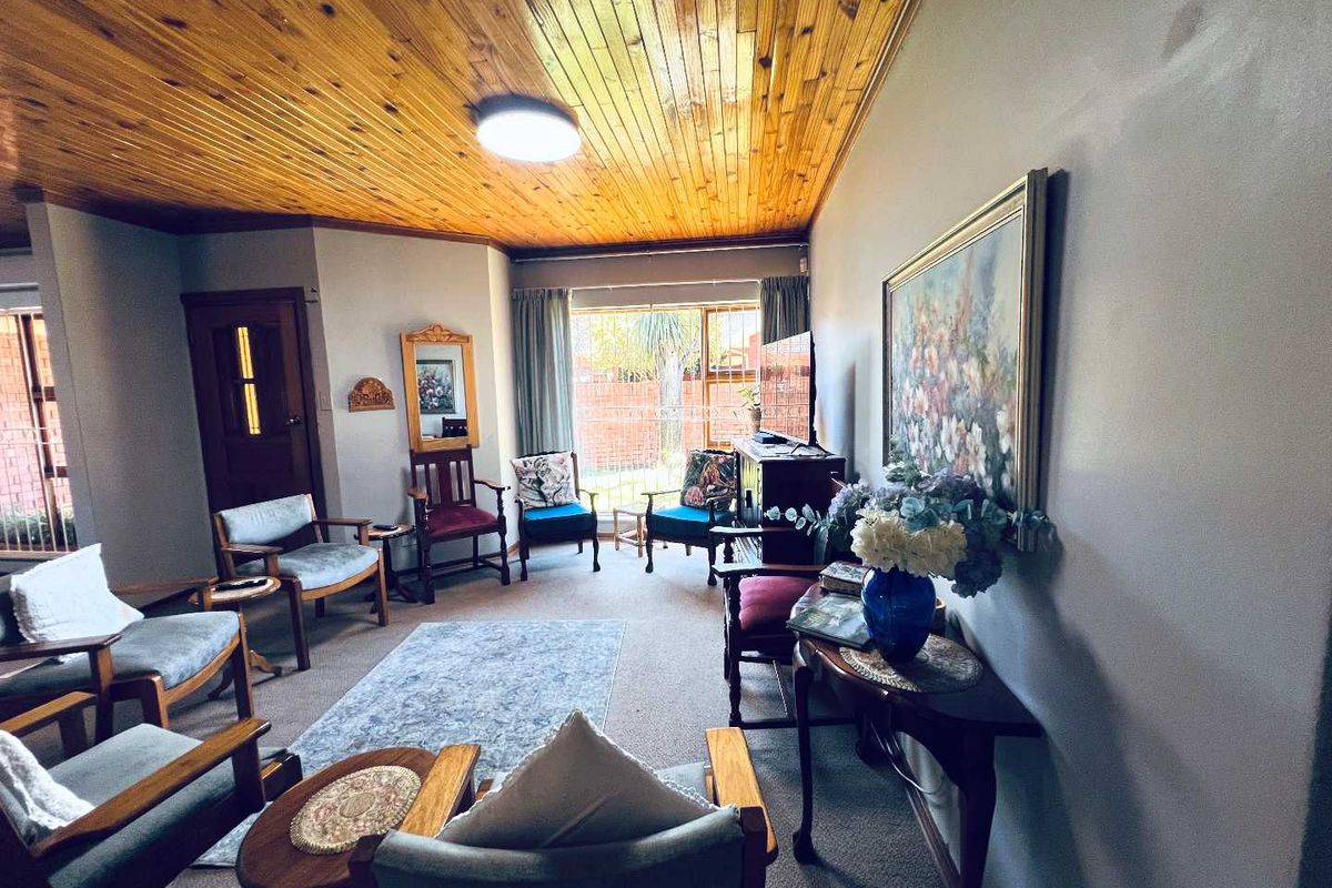 A living room featuring a knotty pine tongue and groove ceiling, carpeted flooring, and large windows providing natural light.