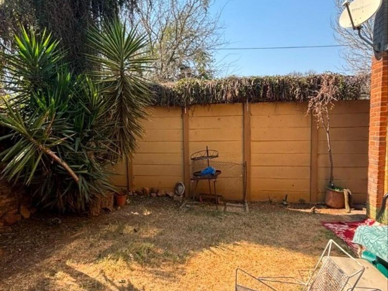A rear garden area featuring a precast concrete boundary wall and established vegetation, requiring landscaping maintenance.
