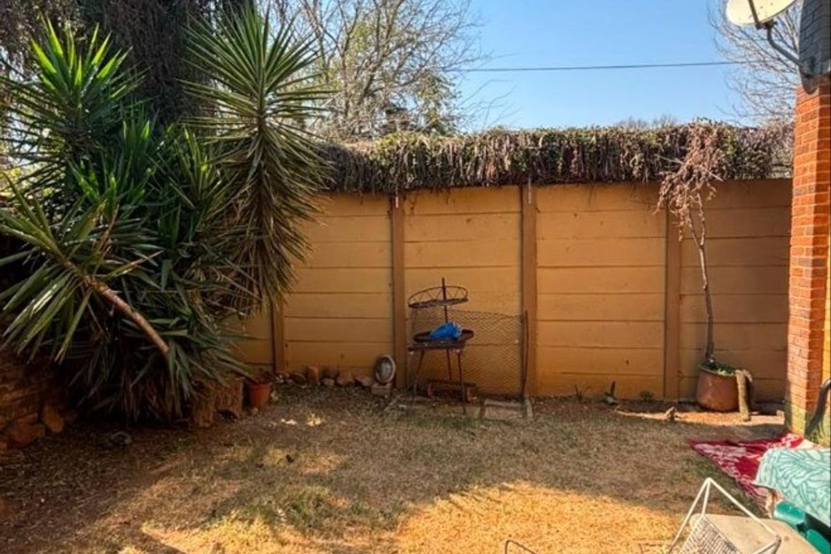 A rear garden area featuring a precast concrete boundary wall and established vegetation, requiring landscaping maintenance.