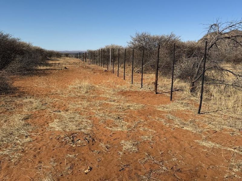 A view of the agricultural land featuring a long stretch of perimeter fencing with metal posts across the dry, open terrain.