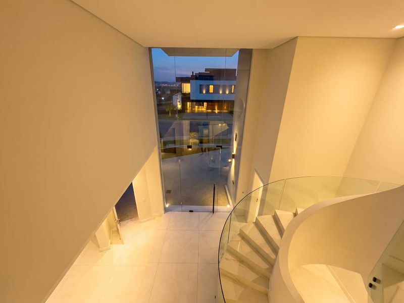 Modern double-volume entrance hall featuring a striking curved staircase with glass balustrade and expansive floor-to-ceiling glass windows overlooking the exterior.