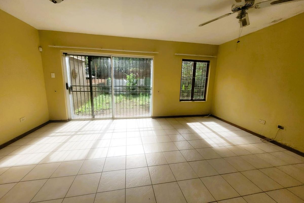 An empty living room featuring tiled flooring, a ceiling fan, and sliding glass doors with security bars leading to the rear garden.