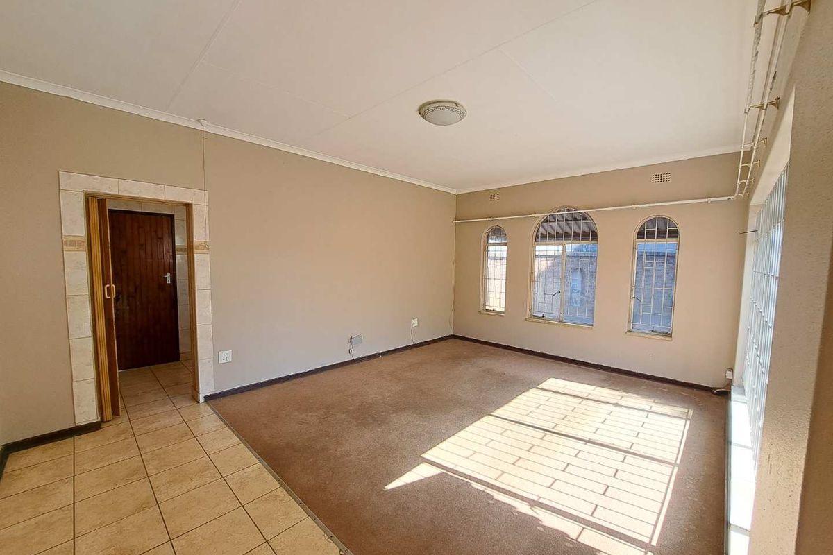 Spacious living area featuring arched windows with security bars, neutral wall tones, and a combination of tiled and carpeted flooring.