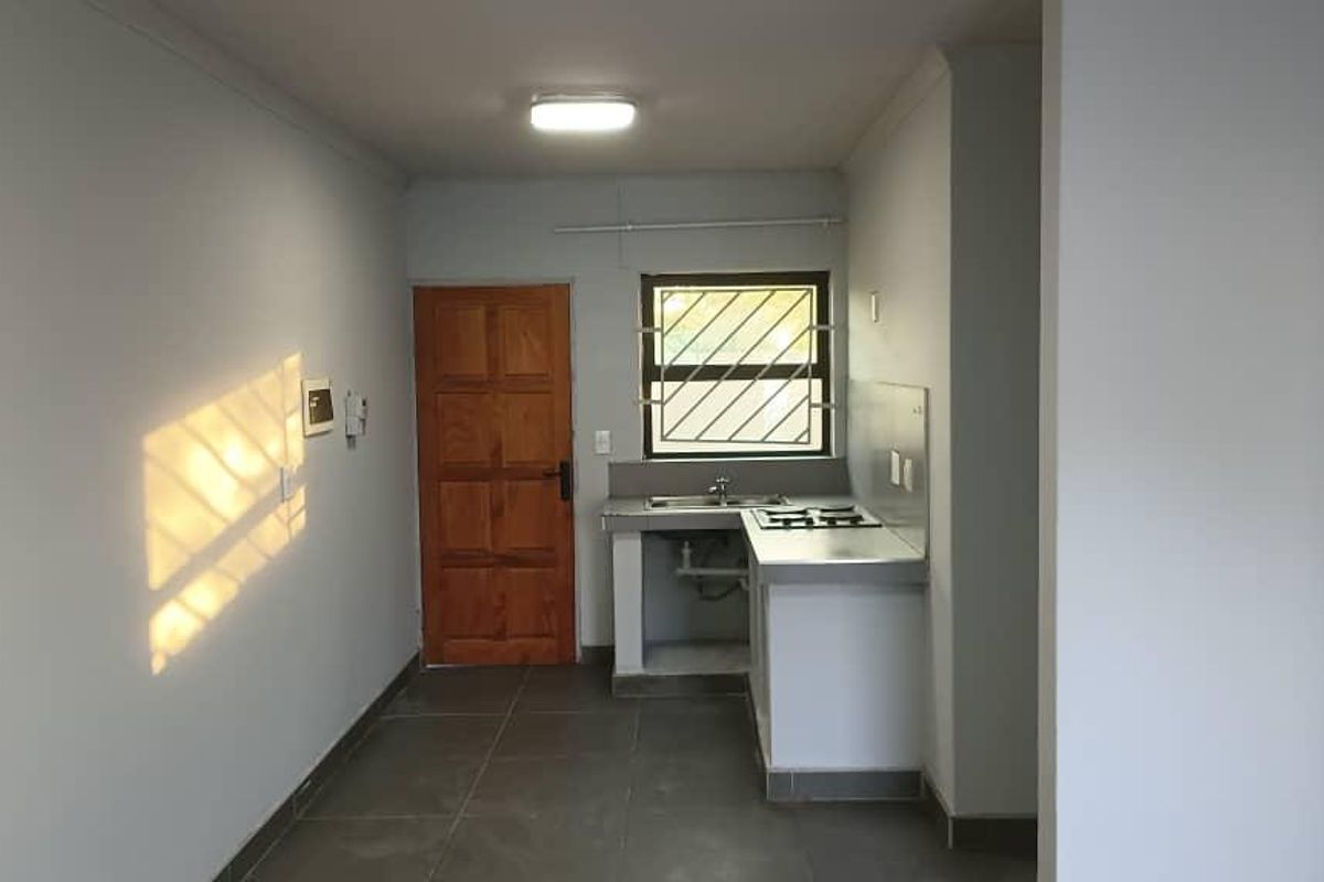 A compact, functional kitchen area featuring tiled flooring, a built-in sink, and a hob, with direct access to an exterior wooden door.