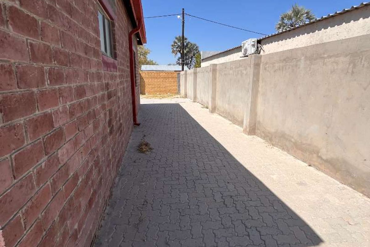 A side exterior walkway featuring brick wall construction, paved ground surface, and a perimeter boundary wall.