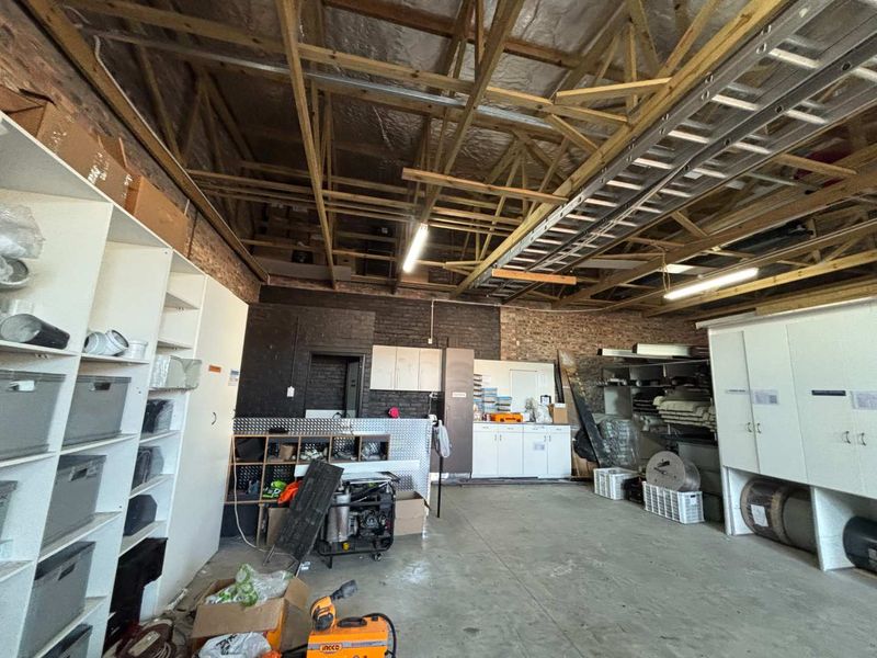 A functional utility or workshop space featuring exposed timber roof trusses, brick walls, concrete flooring, and integrated storage cabinetry.