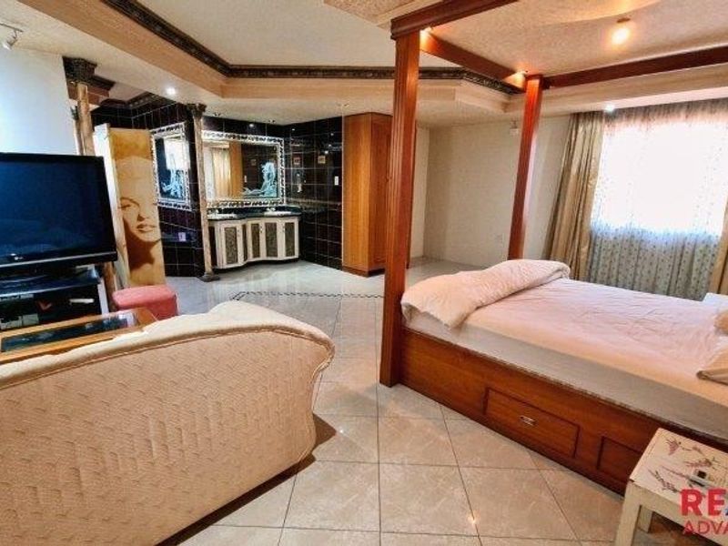 Spacious bedroom featuring tiled flooring, a built-in vanity area with dark tiling, and a recessed ceiling with integrated lighting.