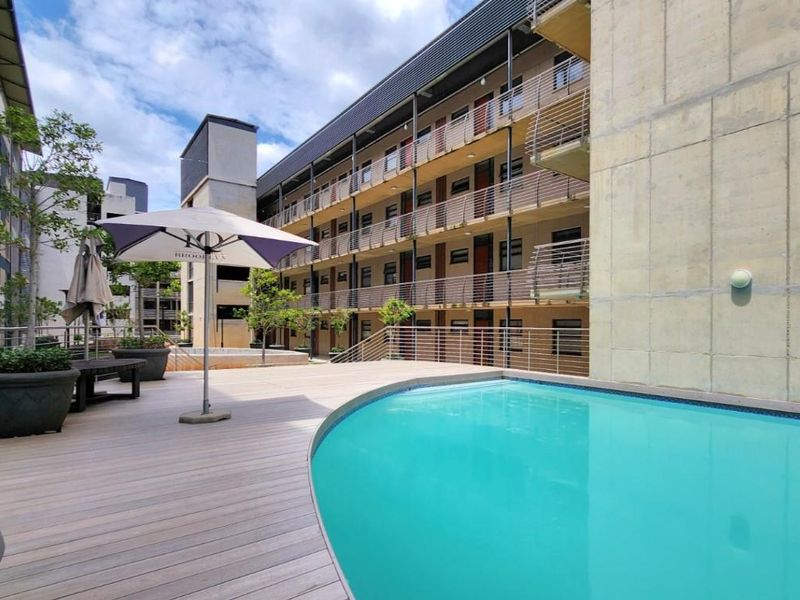 Communal swimming pool area featuring timber decking, modern metal balustrades, and views of the apartment complex facade.
