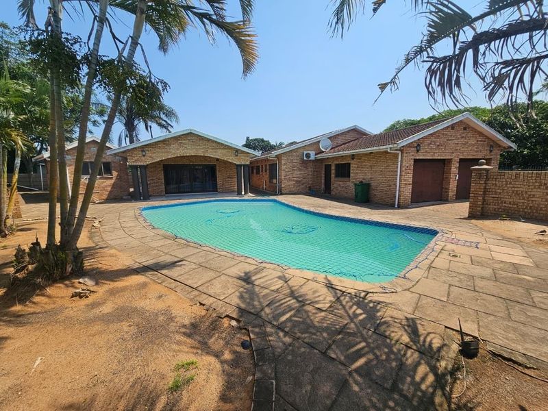 Exterior view of a brick house featuring a swimming pool with a safety net, paved patio area, and a double garage.