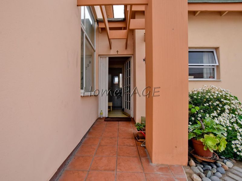 A covered entrance porch featuring terracotta tiled flooring, a timber pergola structure, and a glass-panelled front door leading into the residence.