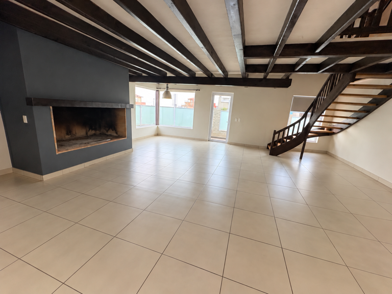 Spacious open-plan living area featuring exposed timber ceiling beams, a large built-in fireplace, tiled flooring, and a feature timber staircase leading to the upper level.