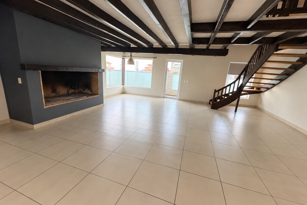 Spacious open-plan living area featuring exposed timber ceiling beams, a large built-in fireplace, tiled flooring, and a feature timber staircase leading to the upper level.