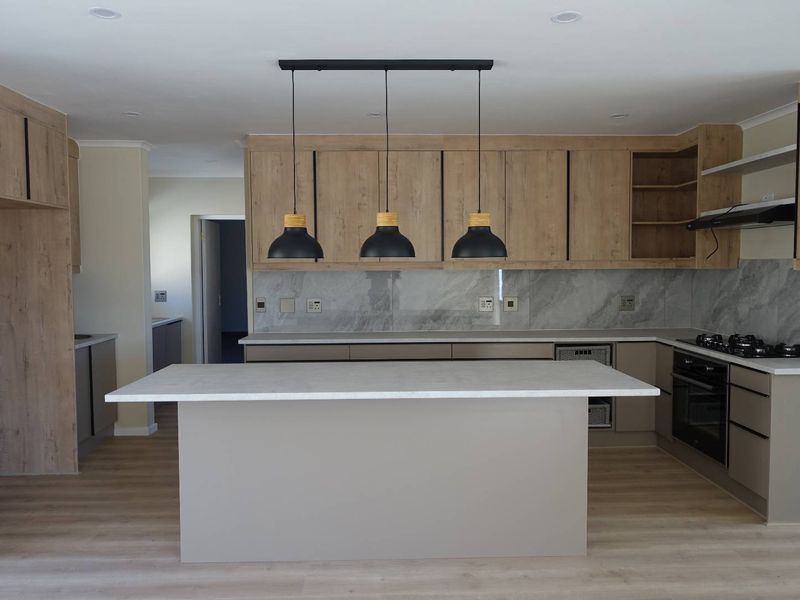 Modern kitchen featuring a central island, light wood cabinetry, stone countertops, integrated appliances, and contemporary pendant lighting in a clean, open-plan layout.