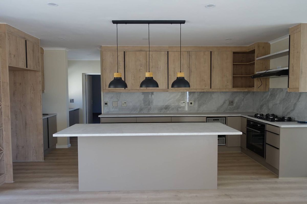 Modern kitchen featuring a central island, light wood cabinetry, stone countertops, integrated appliances, and contemporary pendant lighting in a clean, open-plan layout.