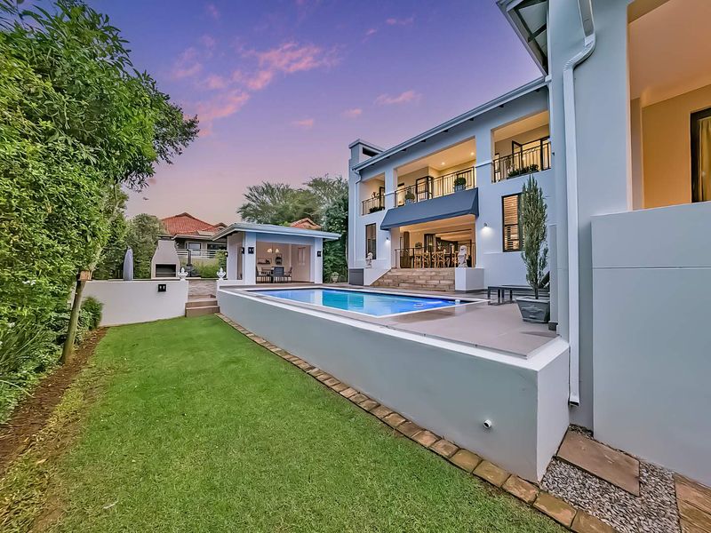 A beautifully maintained rear exterior featuring a swimming pool, covered patio, balcony, and a built-in braai area set within a landscaped garden.