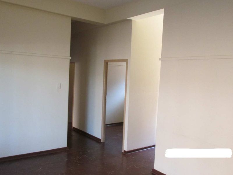 An empty hallway area featuring plain walls, dark flooring, and multiple doorways leading to adjacent rooms.