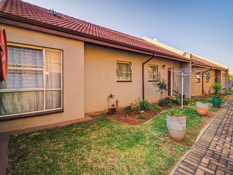 Rear exterior view of the townhouse featuring a tiled roof, paved walkway, and small garden area with an installed fire hose reel.