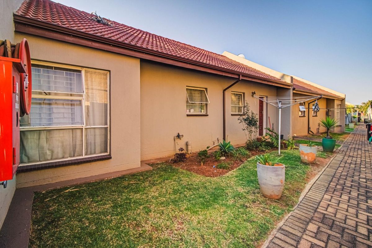 Rear exterior view of the townhouse featuring a tiled roof, paved walkway, and small garden area with an installed fire hose reel.