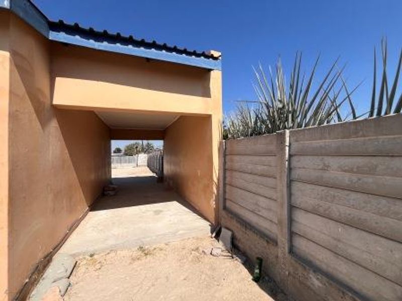 A covered carport area featuring a concrete driveway and a precast concrete boundary wall, showing signs of weathering and wear.