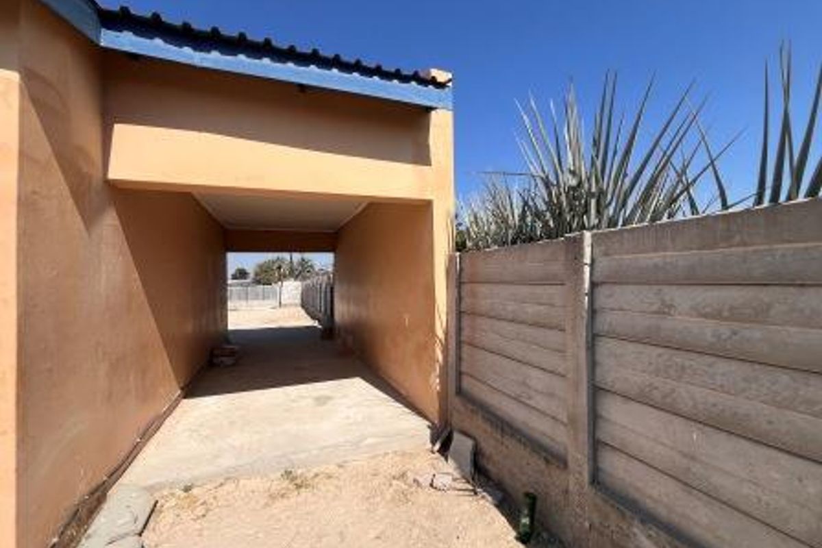A covered carport area featuring a concrete driveway and a precast concrete boundary wall, showing signs of weathering and wear.
