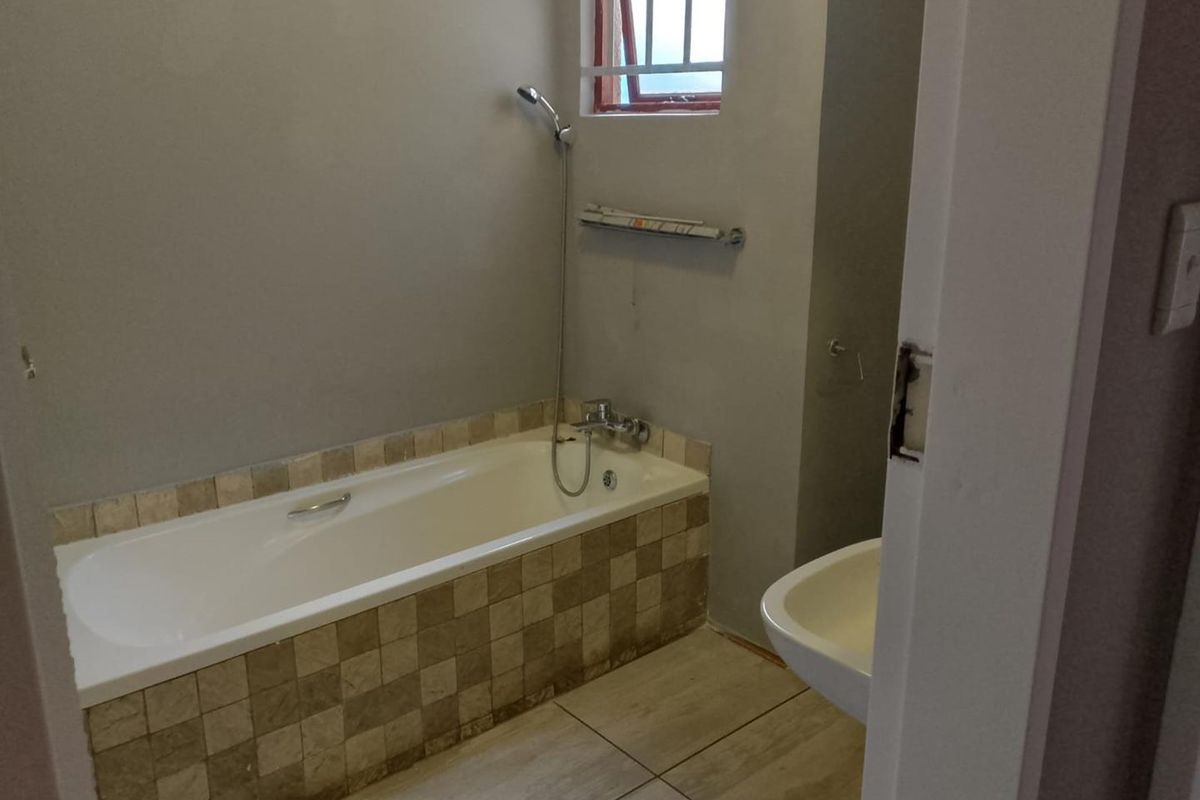 A functional bathroom featuring a tiled bathtub with a handheld shower attachment, a wall-mounted basin, and a window with security bars.