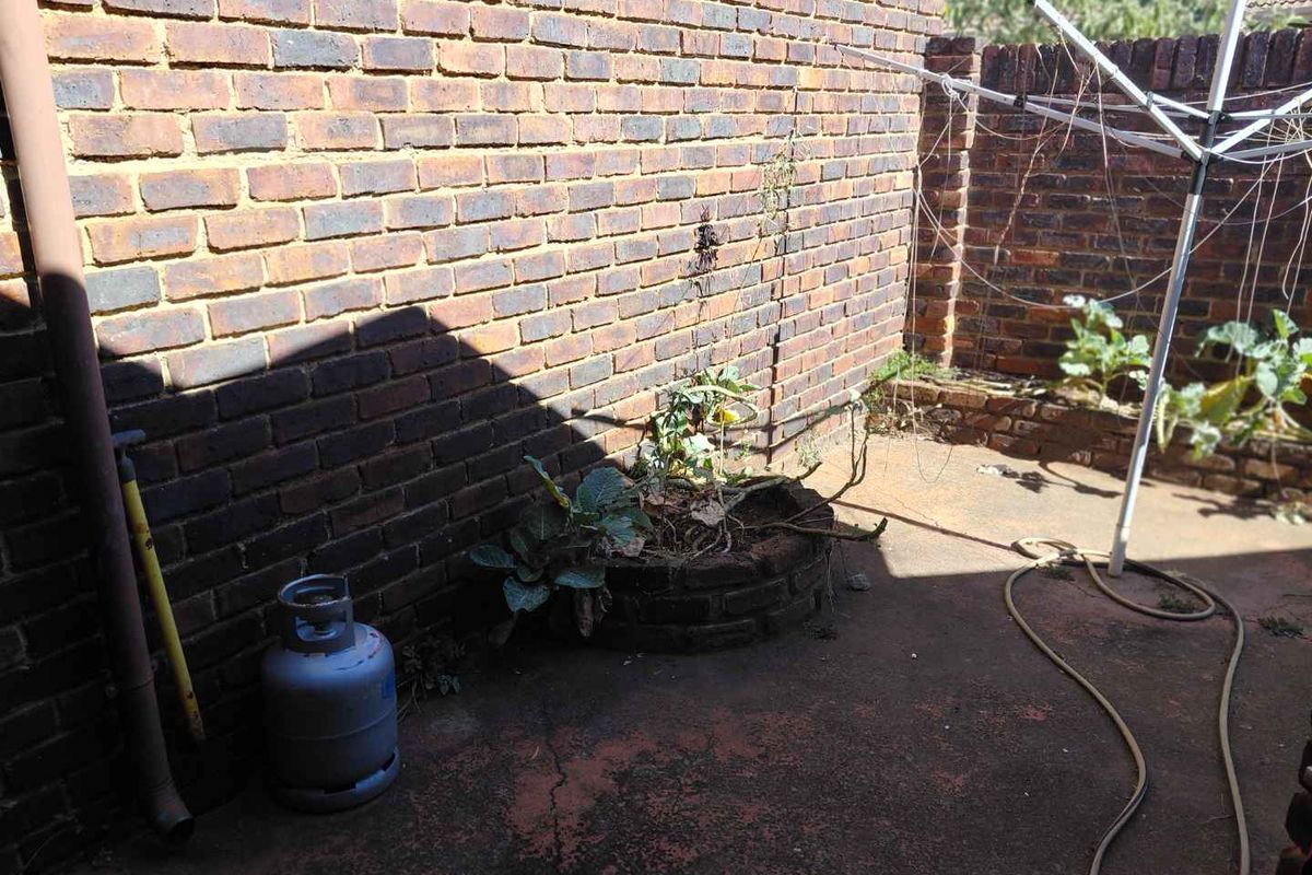 A private rear courtyard area featuring brick boundary walls, concrete paving, and a built-in brick planter box.