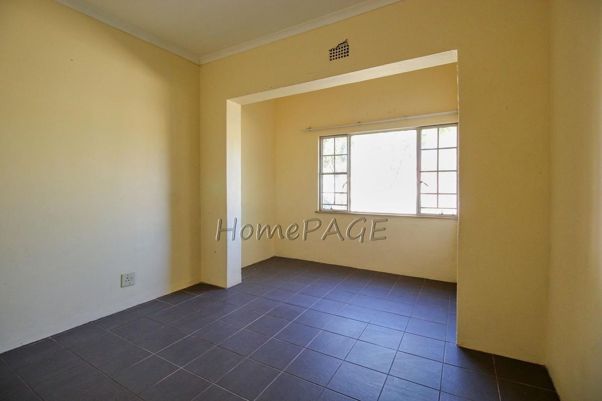 An empty bedroom featuring dark tiled flooring, neutral walls, and a metal-framed window, providing a blank canvas for potential interior design updates.