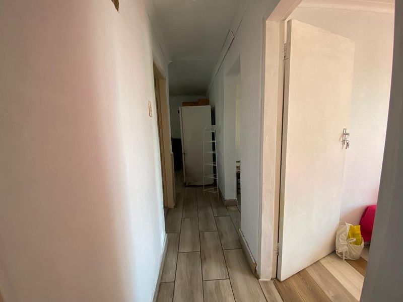 A narrow residential hallway featuring light-toned wood-look floor tiles and white walls, providing access to multiple rooms within the property.