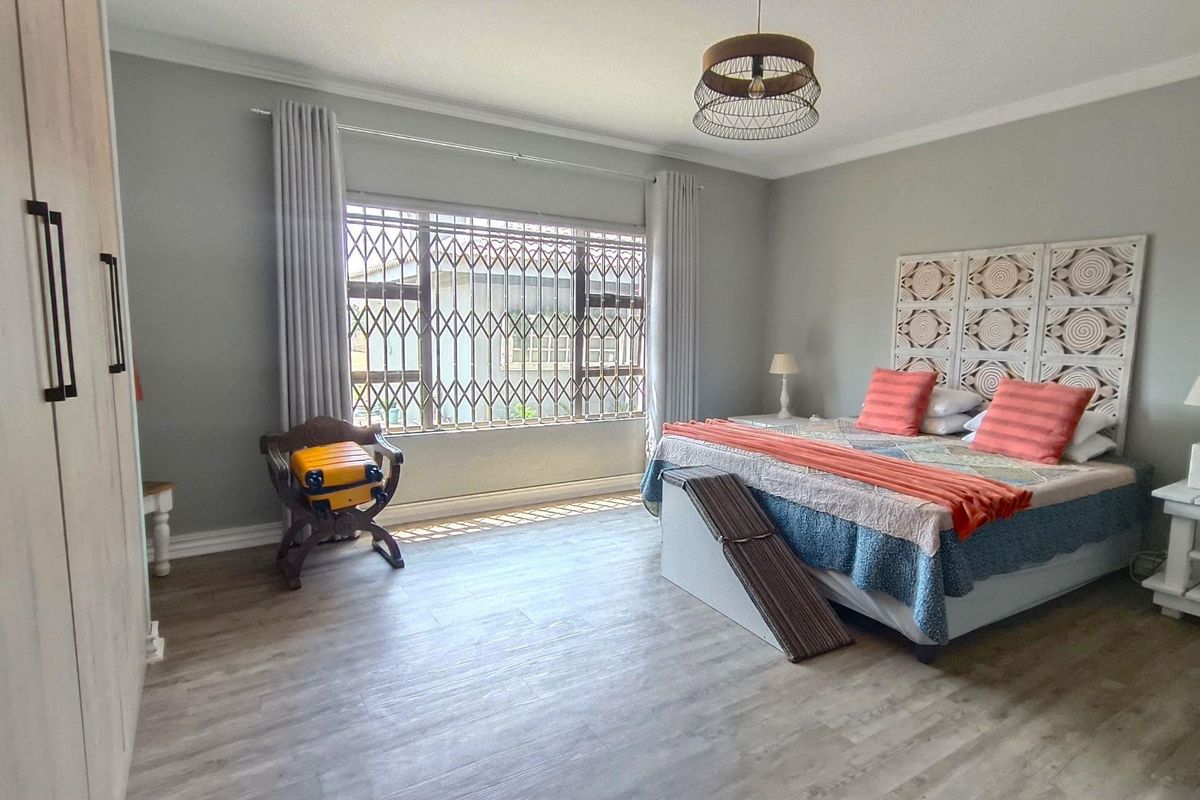 Spacious bedroom featuring light wood-look flooring, built-in cabinetry, and a large window secured with metal security bars.