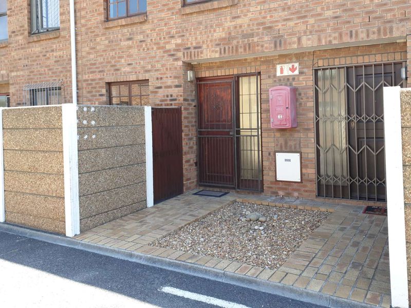 Front entrance of a townhouse featuring a face brick facade, paved walkway, and secure metal gates with an integrated fire safety station.