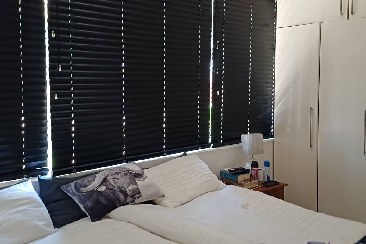 A well-maintained bedroom featuring floor-to-ceiling built-in cupboards and dark venetian blinds for privacy.