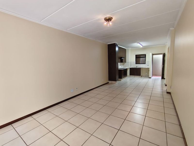An open-plan living and kitchen area featuring tiled flooring, neutral walls, and a functional kitchen layout with built-in cabinetry and appliances.