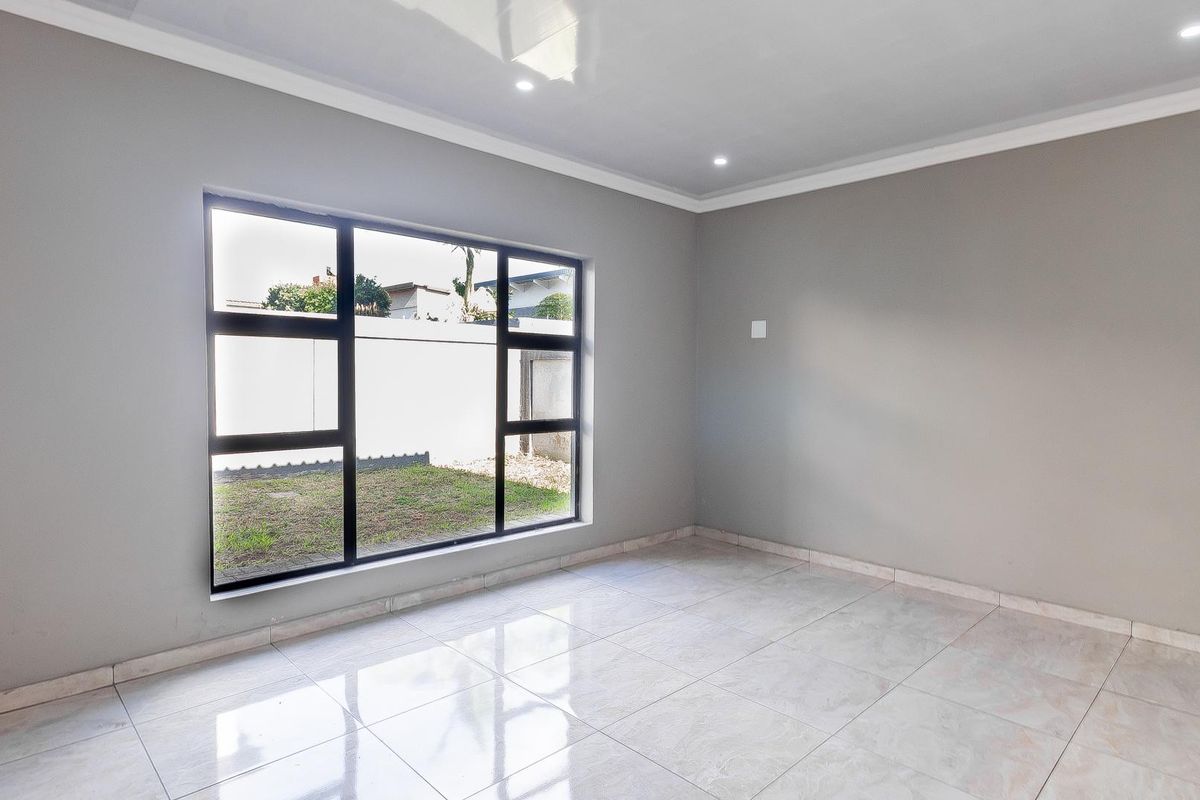 A bright, empty living room featuring neutral grey walls, polished floor tiles, recessed ceiling lighting, and a large window overlooking the garden.