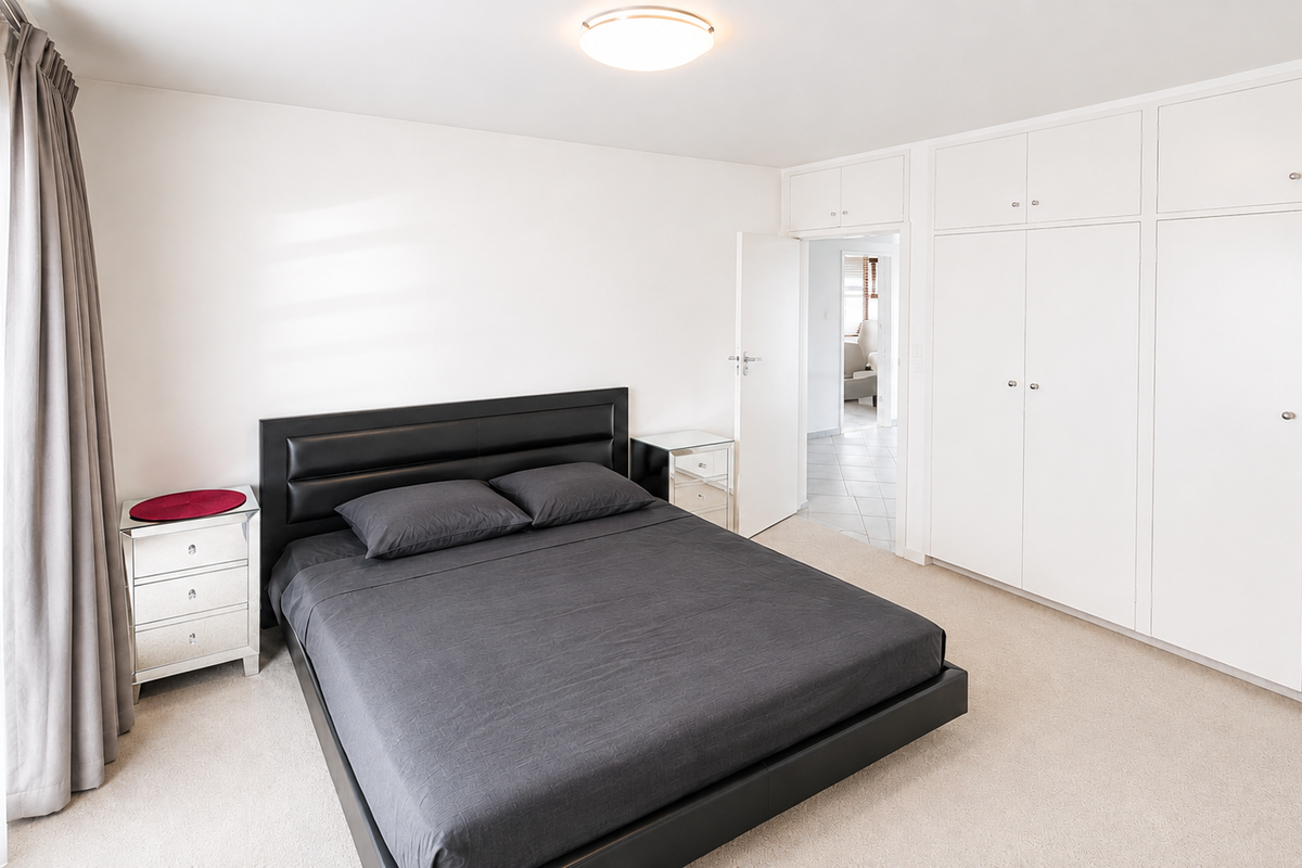 A well-maintained bedroom featuring neutral carpeting, ample built-in cupboard storage, and a bright, clean aesthetic with direct access to an adjoining hallway.