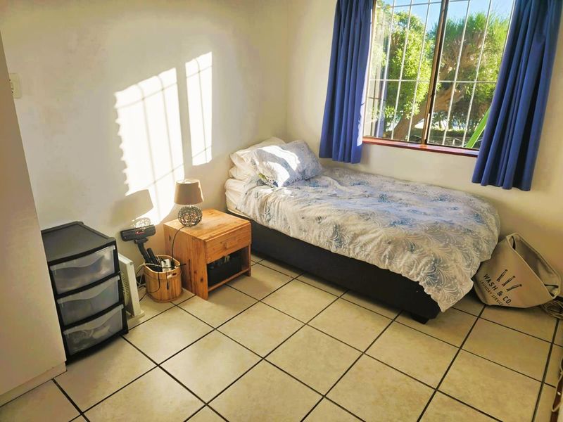 A functional bedroom featuring tiled flooring and a window fitted with security bars, providing natural light and a view of the exterior.