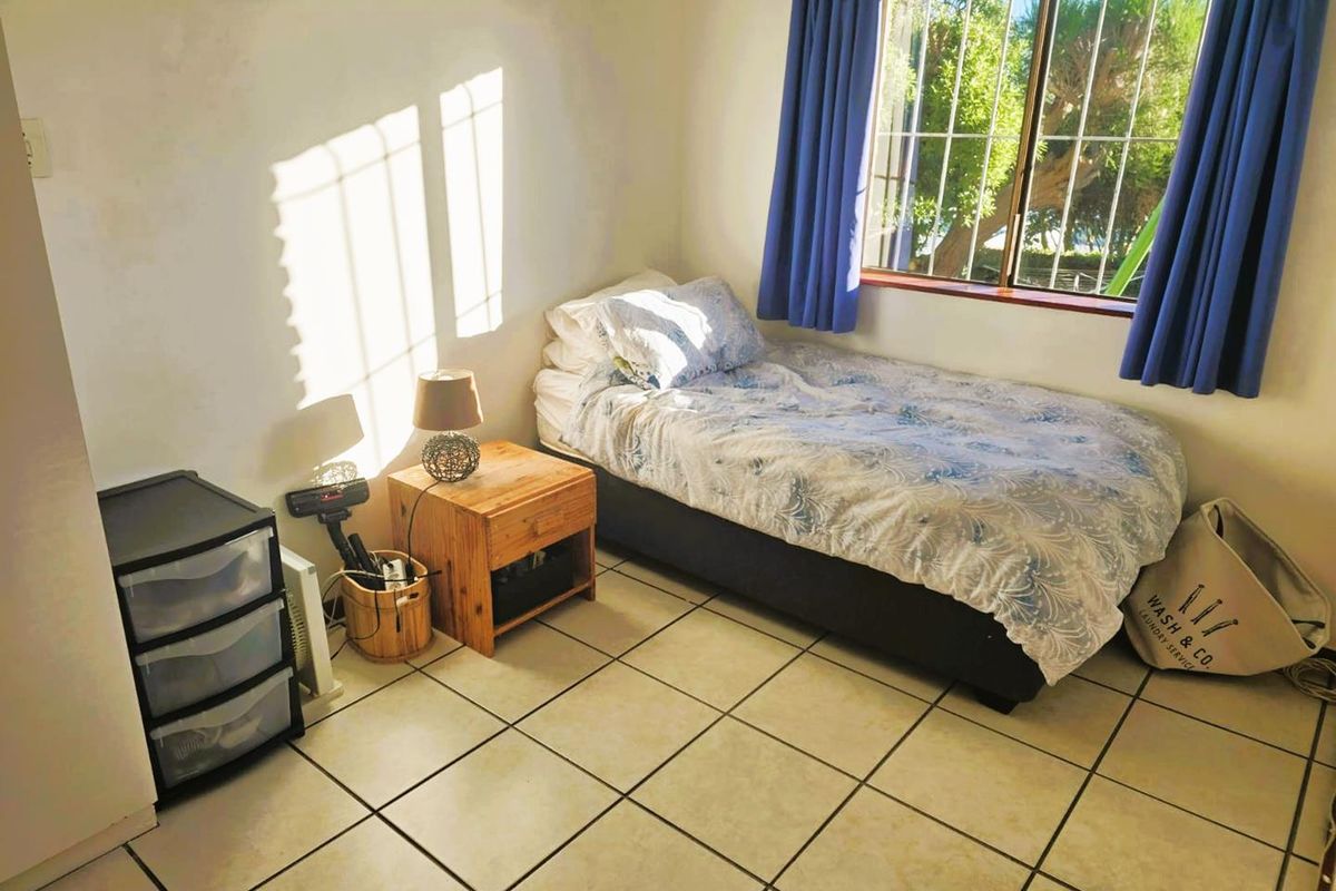 A functional bedroom featuring tiled flooring and a window fitted with security bars, providing natural light and a view of the exterior.
