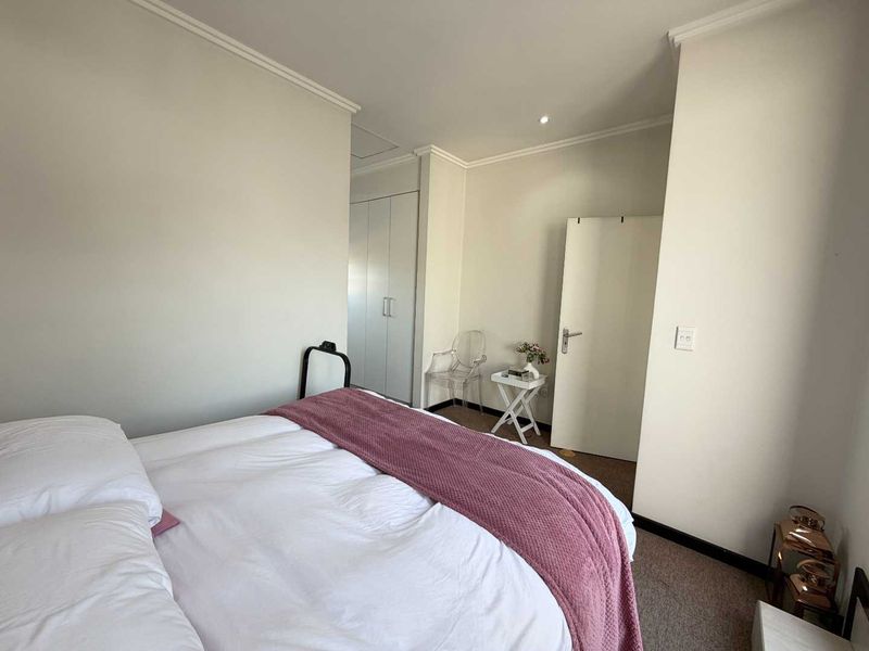 A well-maintained bedroom featuring neutral walls, built-in cupboards, and recessed downlighting, providing a clean and functional living space.