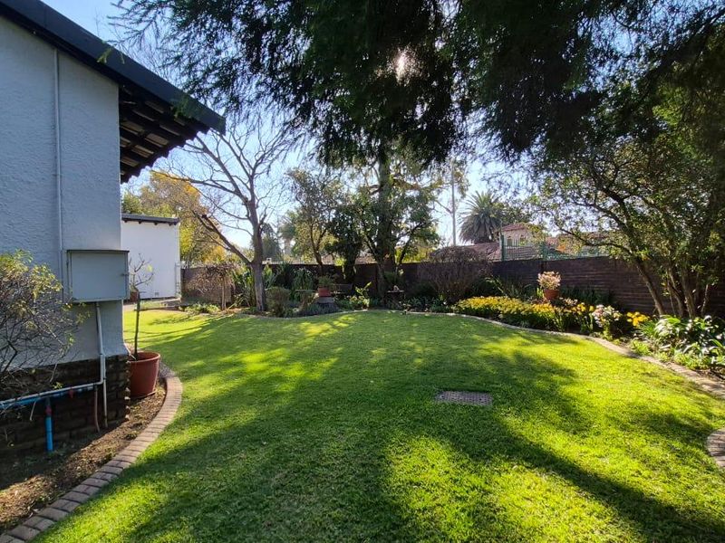 A well-maintained rear garden featuring a lush lawn, established trees, and a secure brick boundary wall.