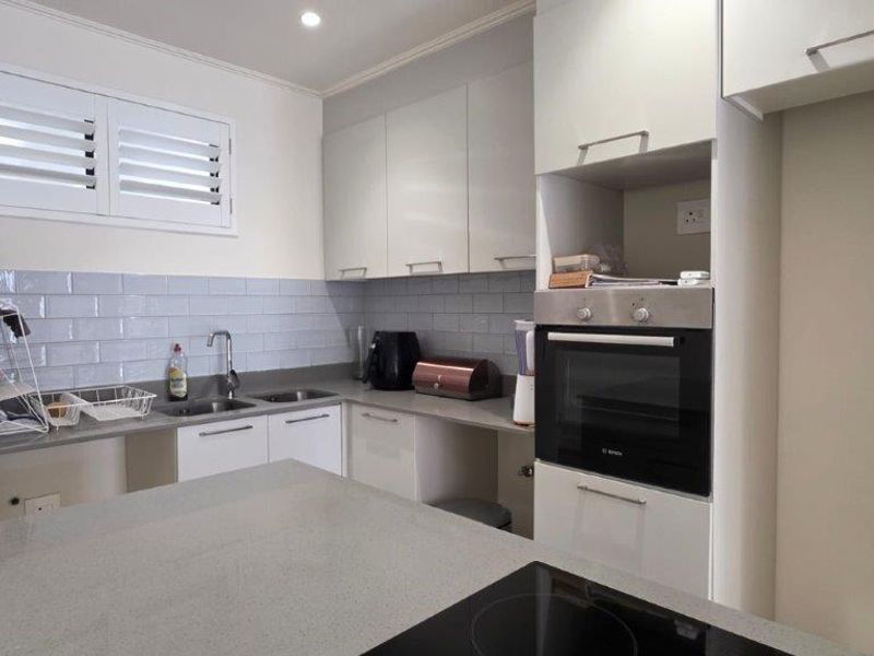 Modern kitchen featuring sleek white cabinetry, stone countertops, subway tile backsplash, built-in oven, and an integrated electric hob.