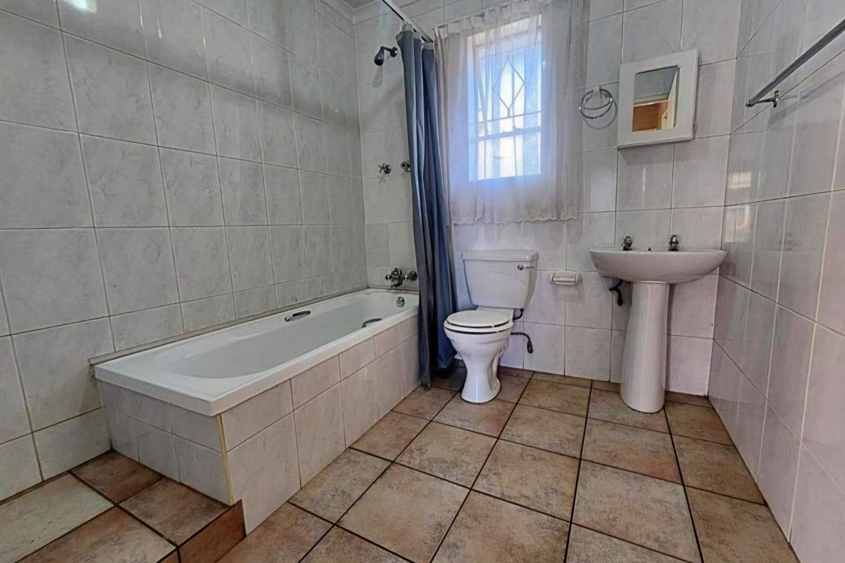 A functional bathroom featuring a bathtub, pedestal basin, and toilet with full-height wall tiling and tiled flooring.