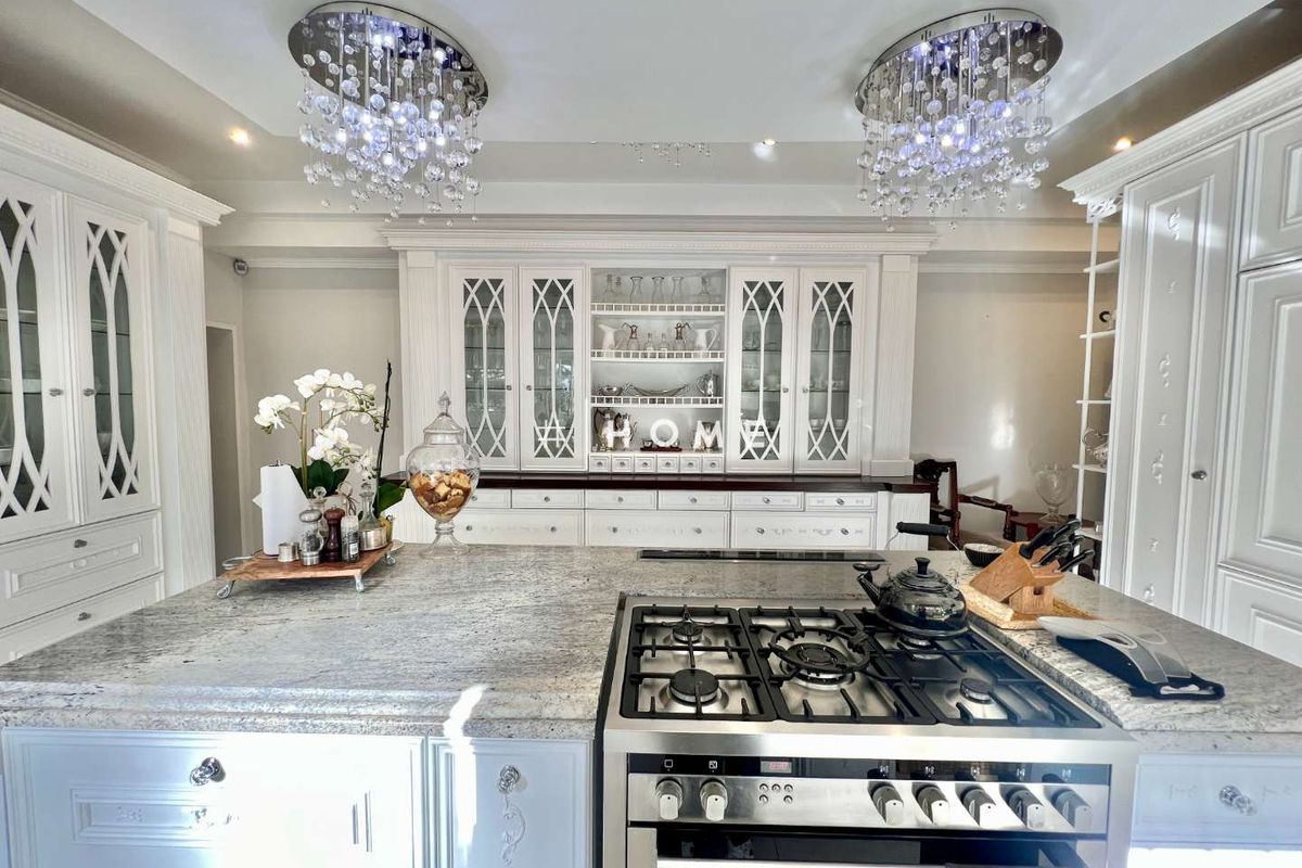 A high-end kitchen featuring custom cabinetry with glass-front displays, a large granite-topped island, and a professional-grade gas range.