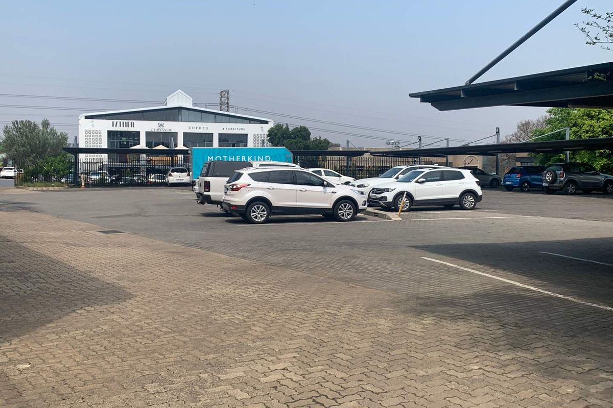 Exterior view of a commercial office property featuring a paved parking lot with covered parking bays and perimeter security fencing.