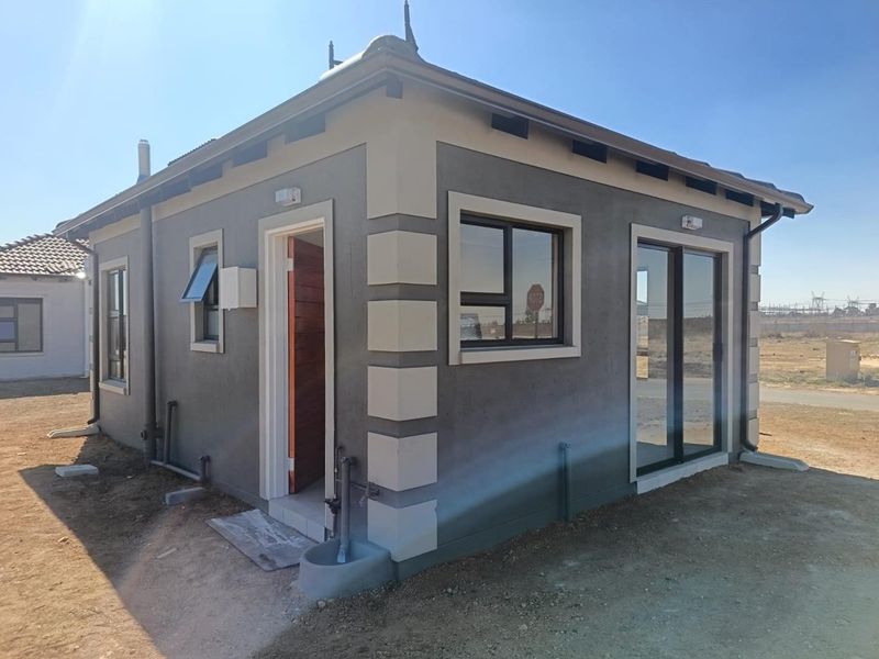 Exterior view of a modern single-story house featuring grey rendered walls with corner detailing, aluminium window frames, and a tiled roof.