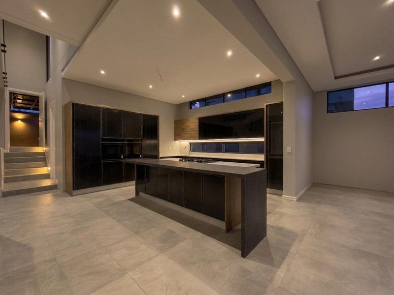 Modern, spacious kitchen featuring dark cabinetry, a large central island with stone countertops, recessed lighting, and sleek tiled flooring in an open-plan layout.