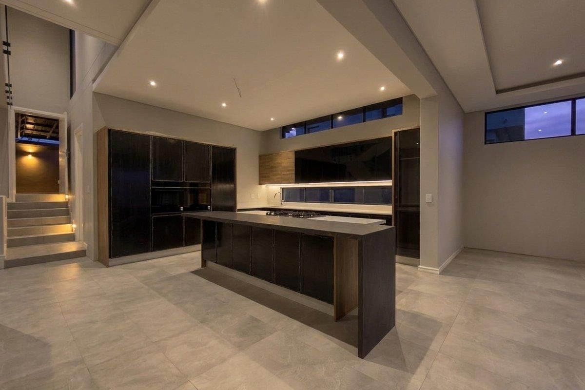 Modern, spacious kitchen featuring dark cabinetry, a large central island with stone countertops, recessed lighting, and sleek tiled flooring in an open-plan layout.