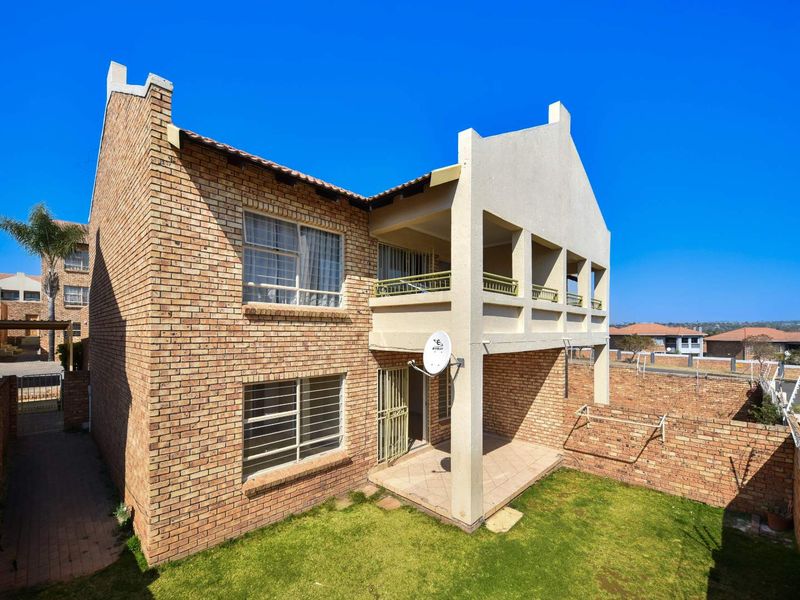 Rear view of a double-story face brick apartment building featuring a ground floor patio, upper-level balcony, and a private garden area.