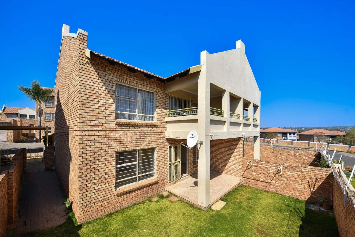 Rear view of a double-story face brick apartment building featuring a ground floor patio, upper-level balcony, and a private garden area.