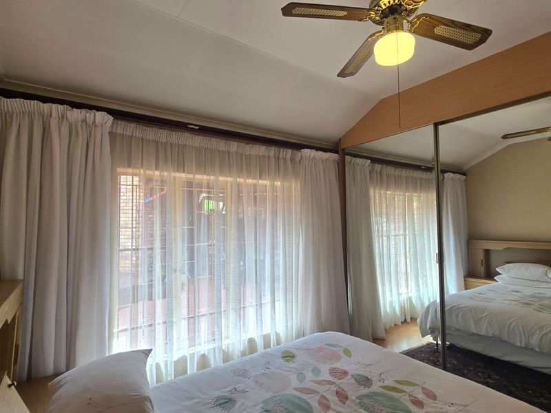 A bedroom featuring a ceiling fan and large built-in wardrobes with mirrored sliding doors, providing ample storage and natural light.